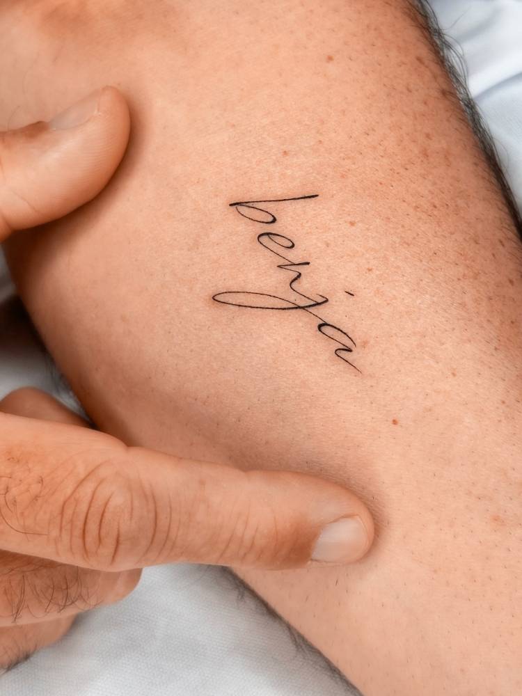 "Benja" lettering tattoo in script font placed on the inner forearm.