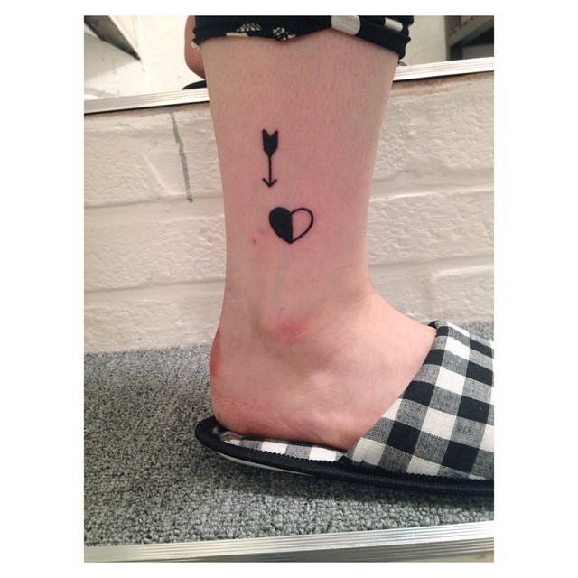 Arrow and heart tattoos in minimalistic style done on the ankle.