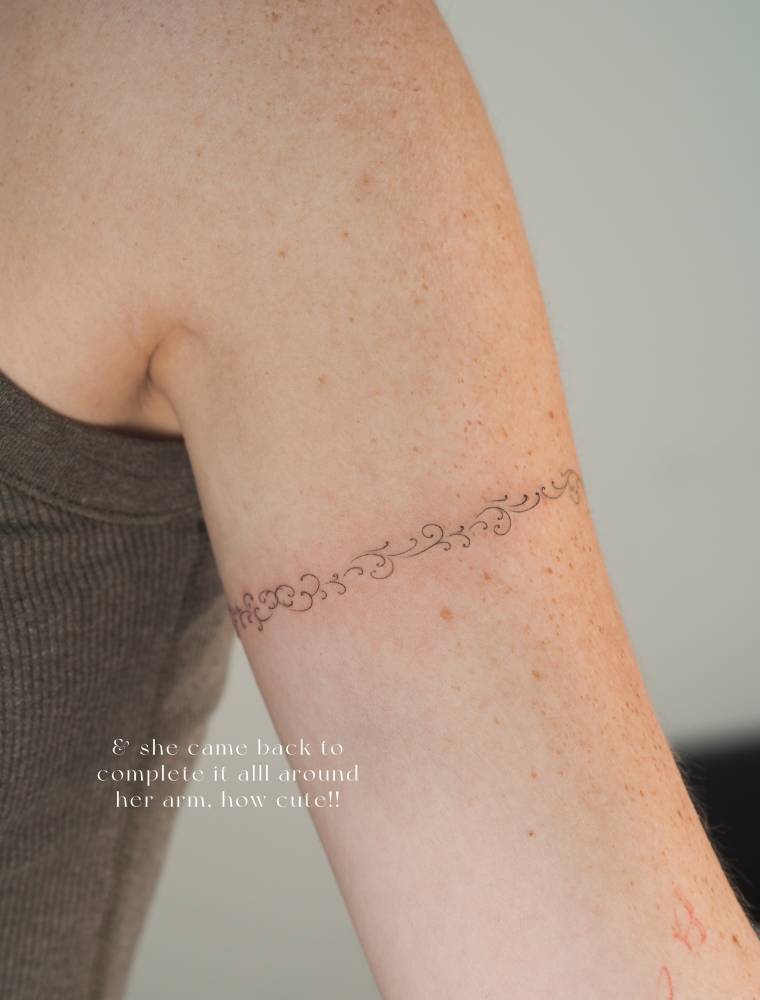 Ornamental bracelet tattoo in fine line style located on the upper arm.