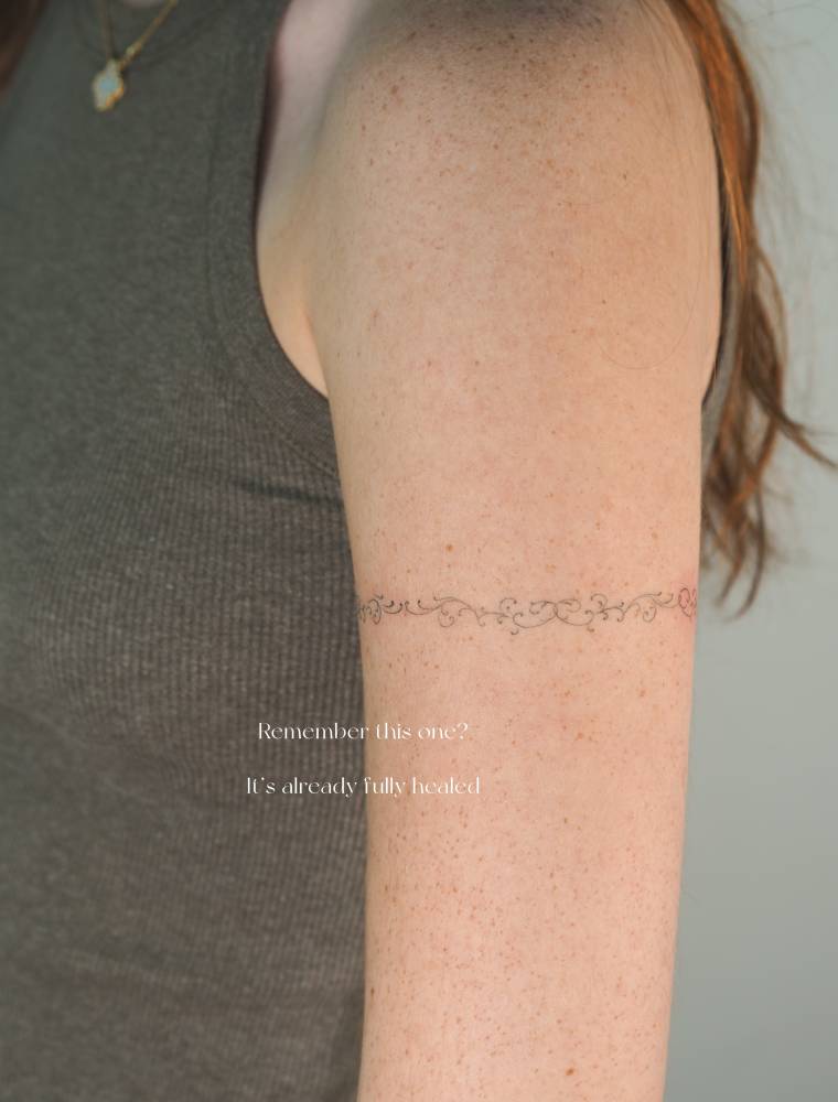 Healed ornamental bracelet tattoo in fine line style located on the upper arm.