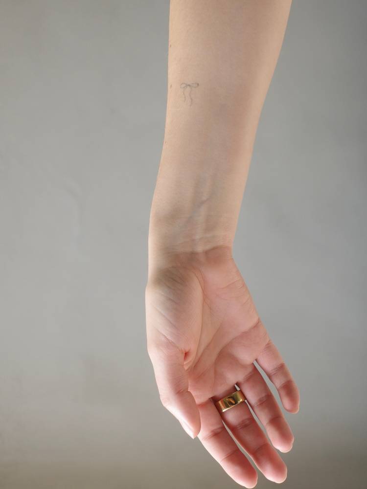 Tiny ribbon tattoo in fine line style done on the inner forearm.
