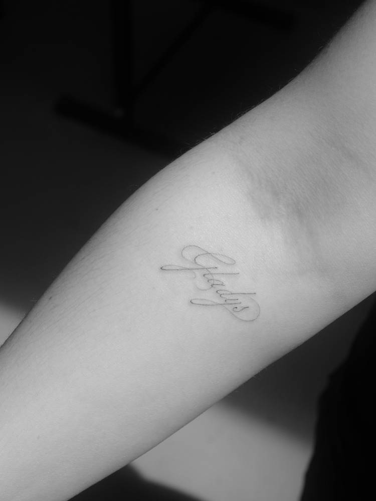 "Gladys" lettering tattoo in script font located on the inner forearm.