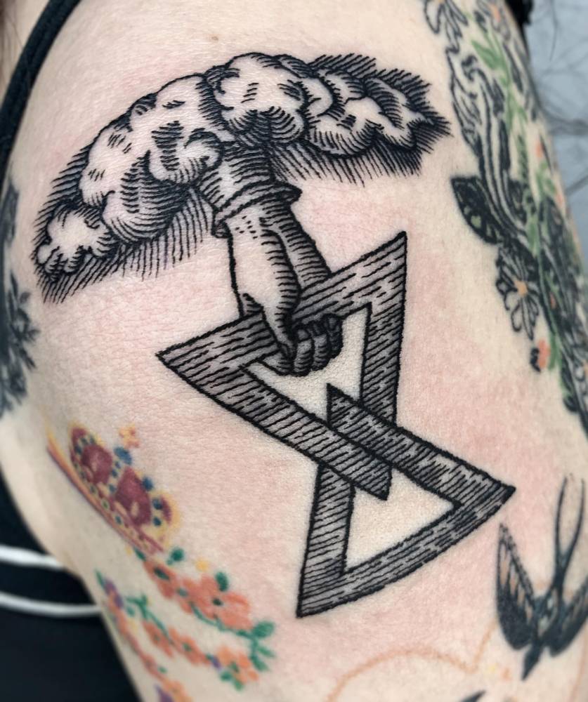 Hand holding intertwined triangle tattooed on the shoulder.