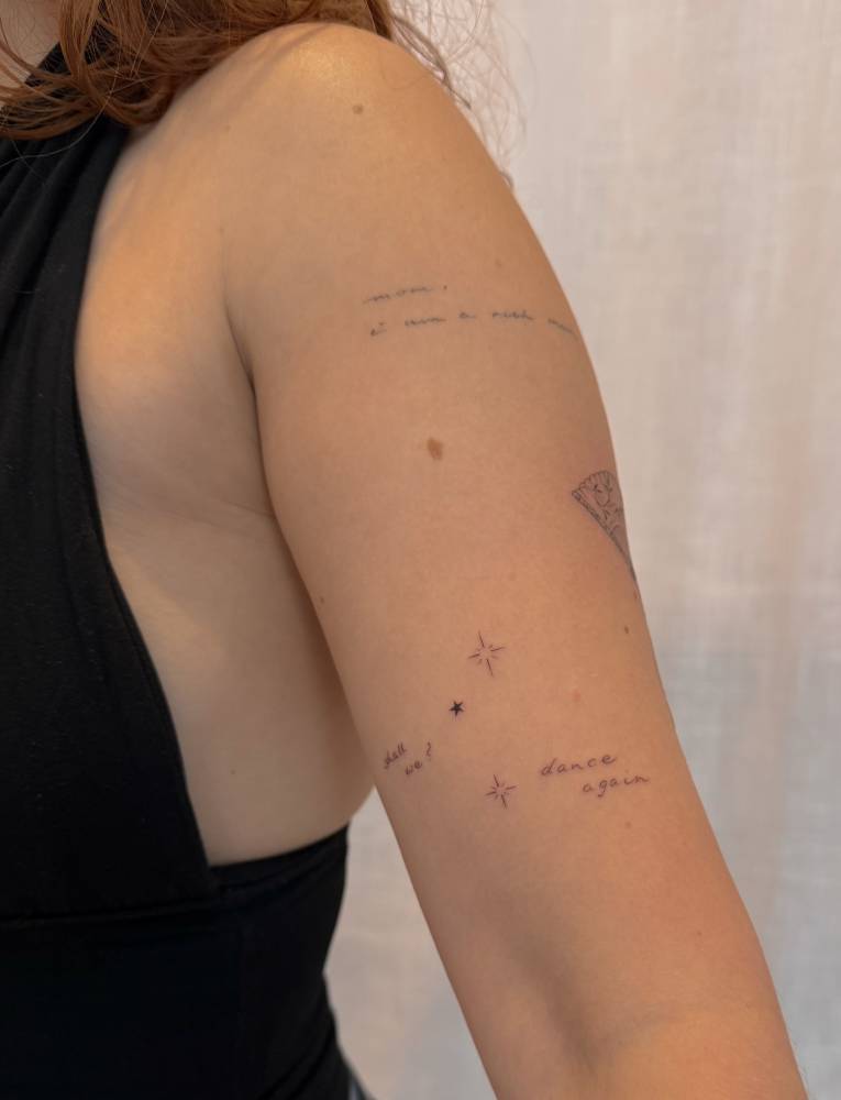 Minimalistic sparkling stars and "dance again" tattoo located on the upper arm.