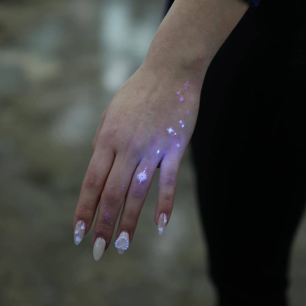 Sparkling stars tattoo in UV ink located on the hand.