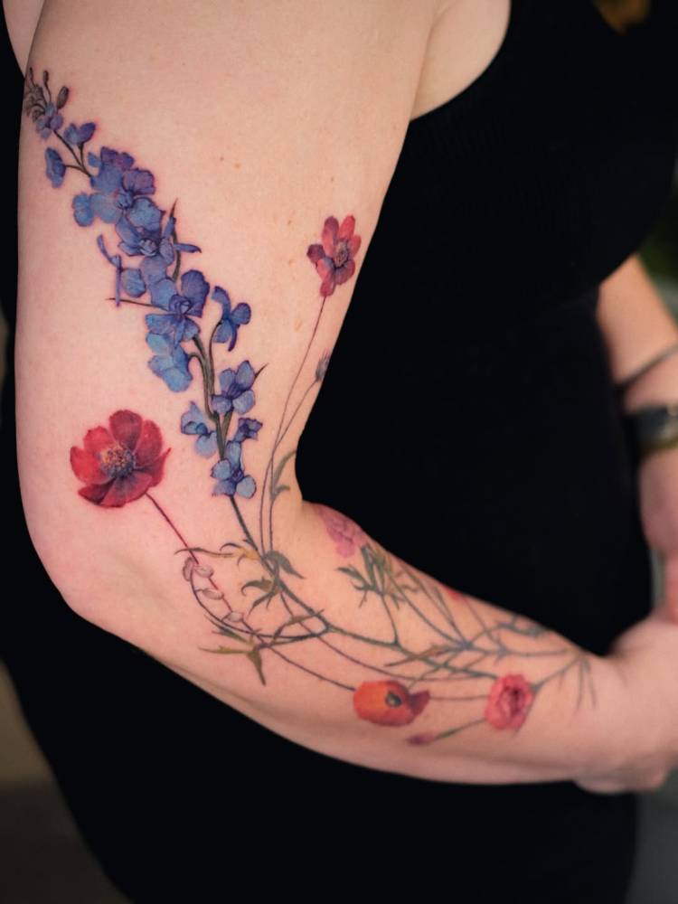 Larkspur and poppies tattooed on the arm, watercolor style.