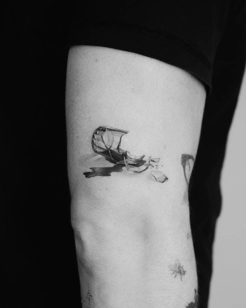 Broken glass tattoo in micro-realistic style located on the upper arm.