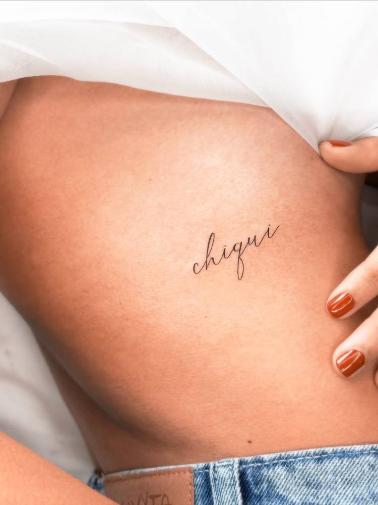 Script font word "chiqui" tattooed on the rib.