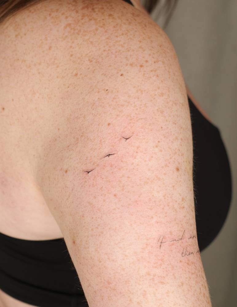 Tiny minimalistic flying birds tattoo located on the upper arm.