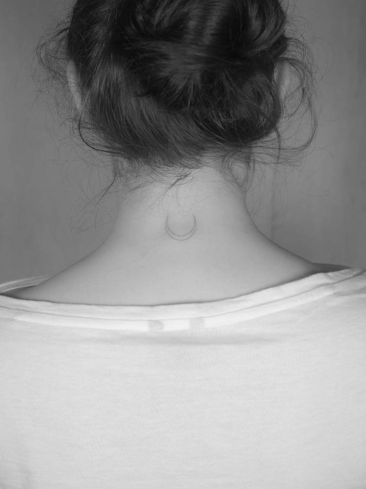 Minimalistic crescent moon tattoo in fine line style located on the back of the neck.