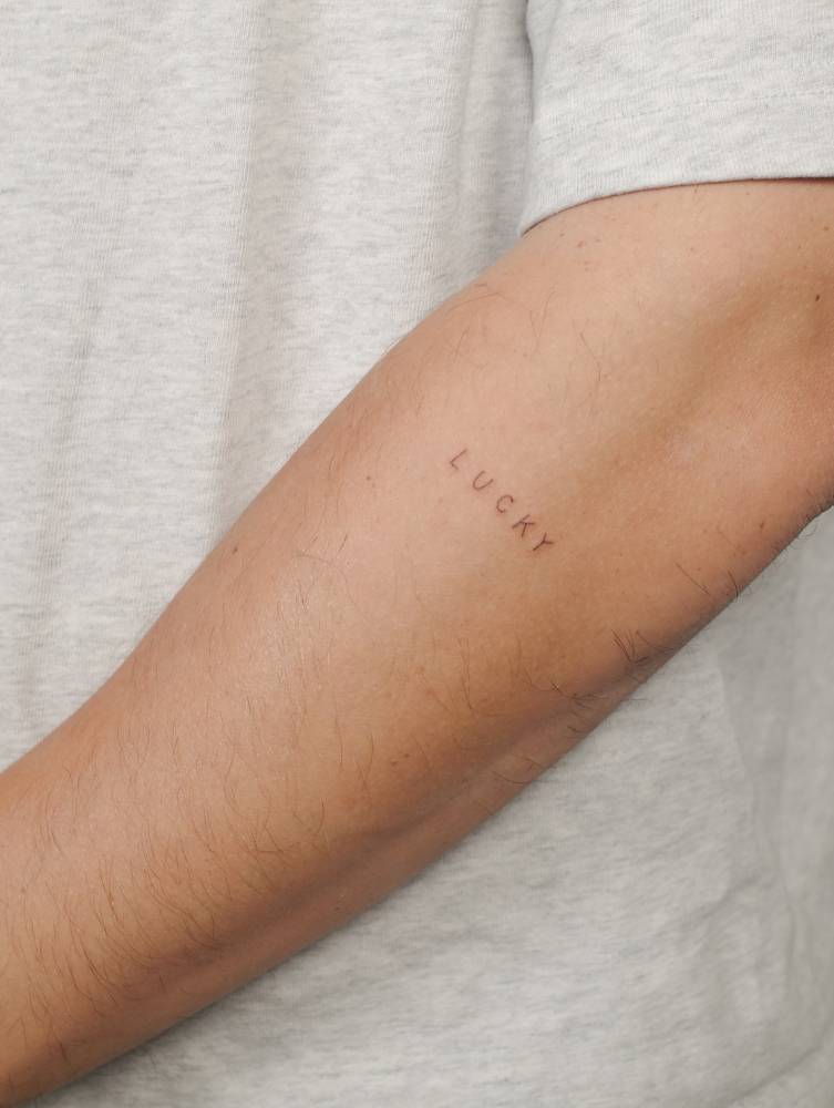 Handwritten font word "lucky" tattoo located on the forearm.