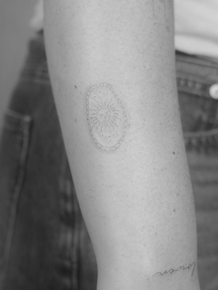 Inti sun tattoo located on the wrist, done in fine line style.
