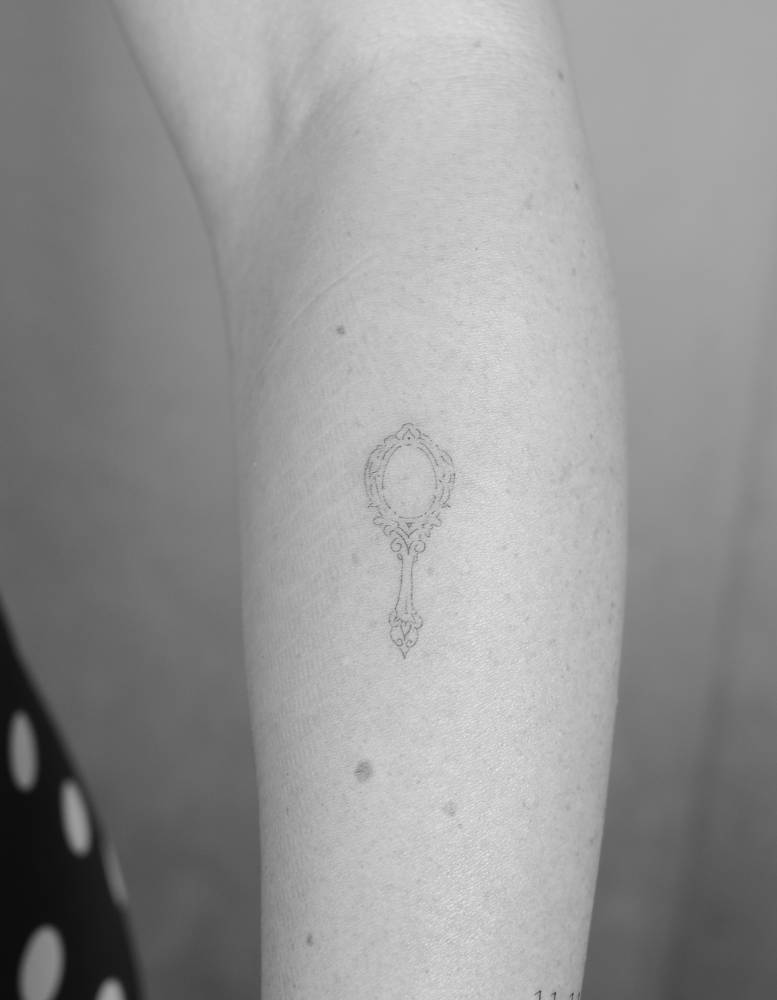 Hand mirror tattooed on the forearm, fine line style.