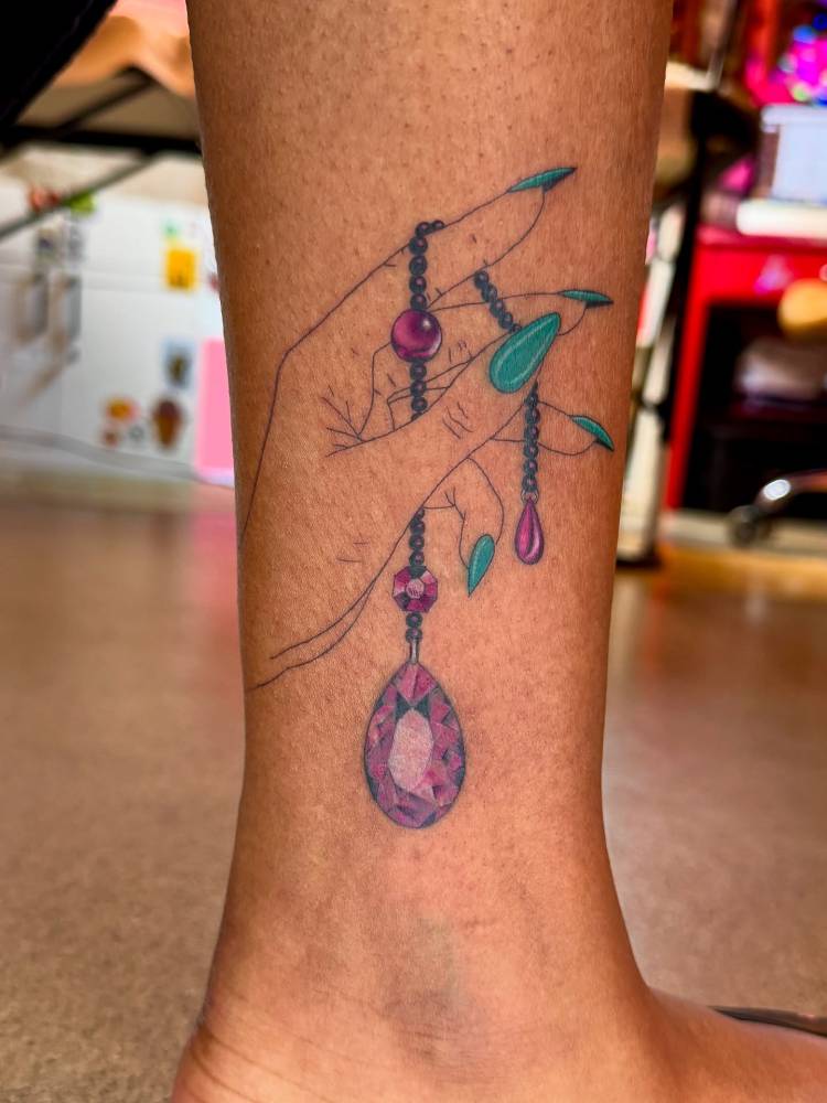 Hand holding an amethyst gem tattooed on the ankle.