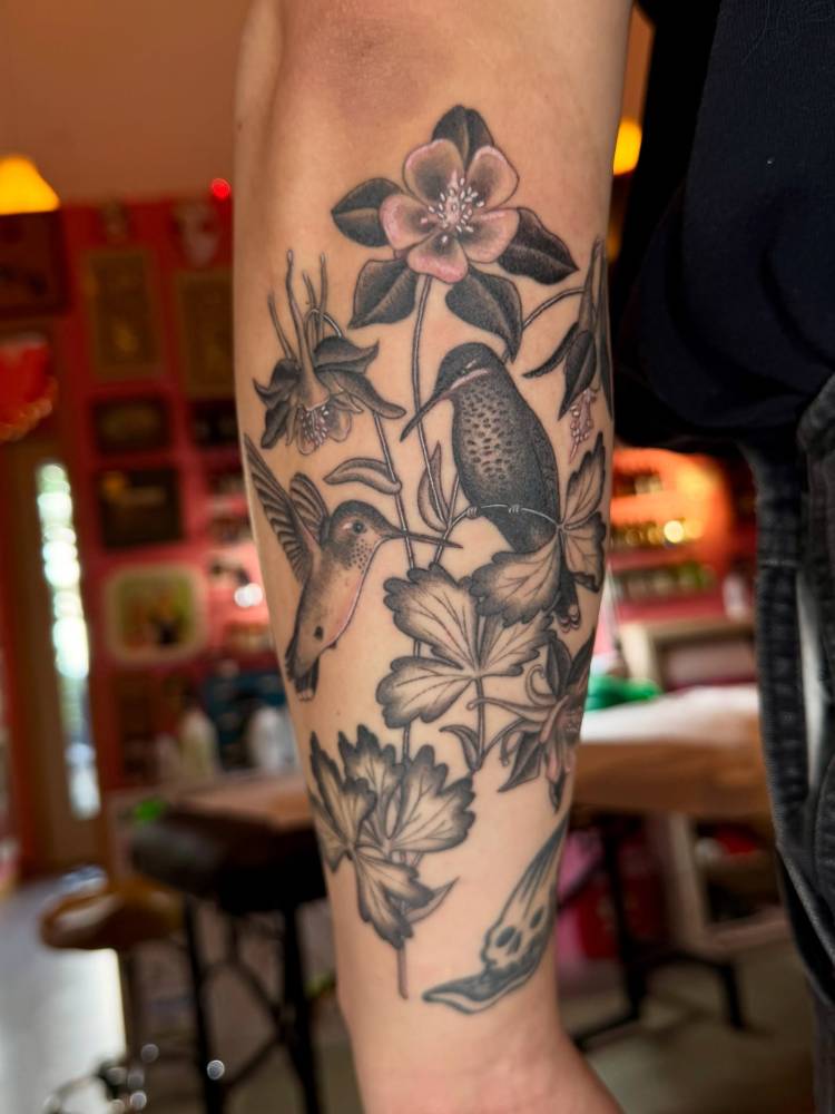 Illustrative style hummingbirds and flowers tattooed on the forearm.