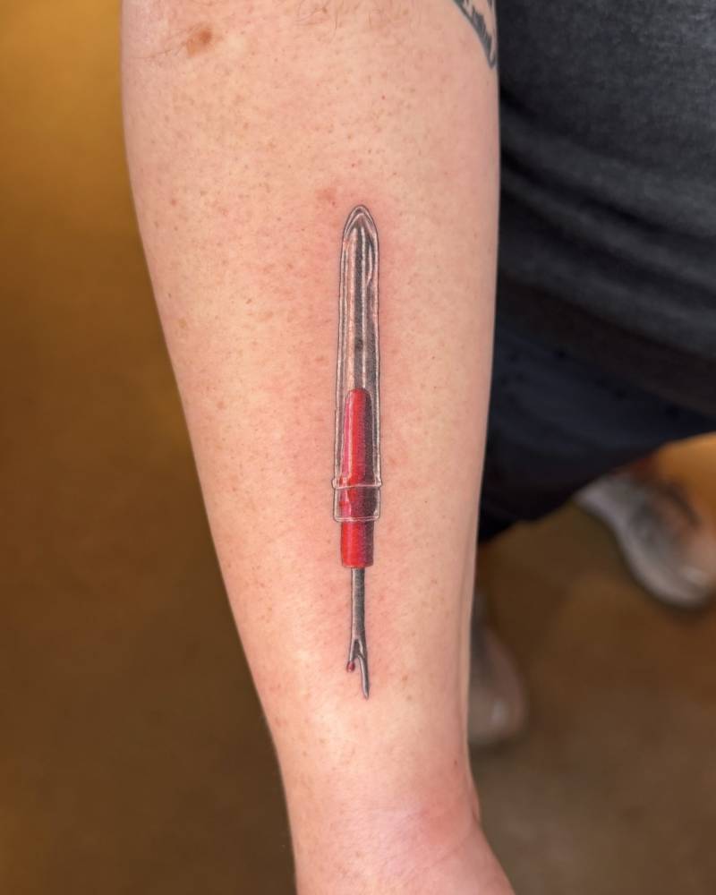 Seam Ripper tattoo in illustrative style located on the forearm.