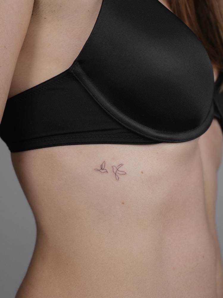 Tiny flying birds tattooed on the rib, minimalistic style.