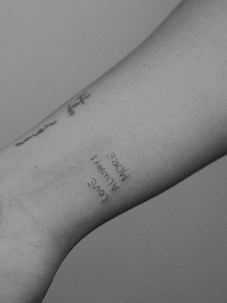 "Love always more" lettering tattoo located on the wrist.