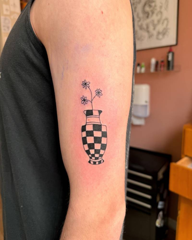 Flowers in a vase tattoo located on the upper arm, illustrative style.