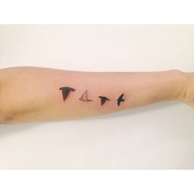 Flying birds tattoo in illustrative style located on the forearm.