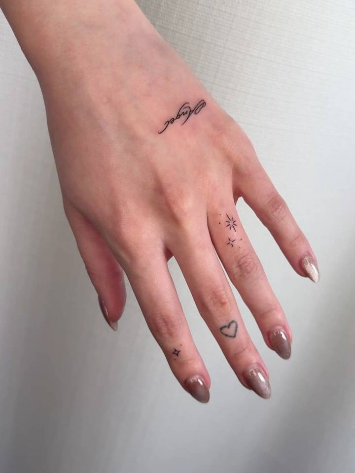 Minimalistic style sparkling stars and word "angel" tattoos located on the hand and fingers.