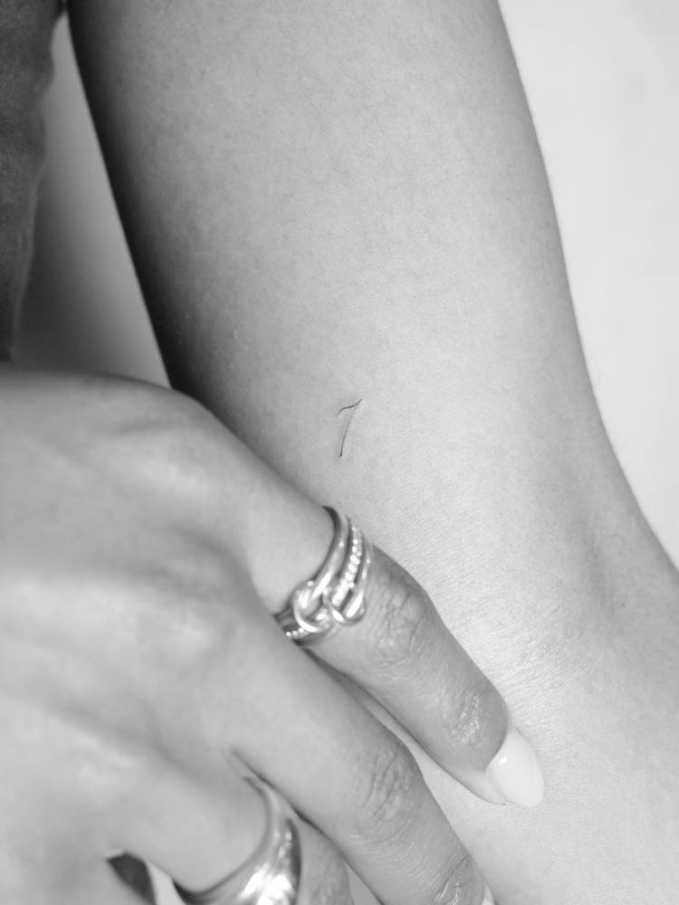 Minimalistic tattoo of the number "7" placed on the inner arm.