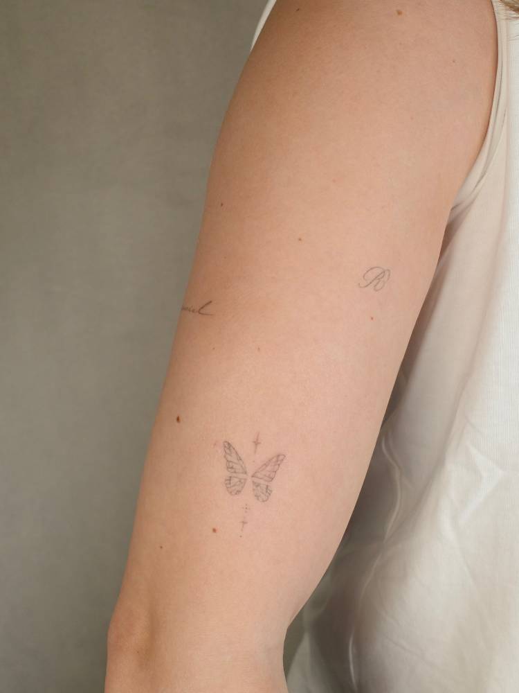 Fine line style butterfly tattoo located on the upper arm.
