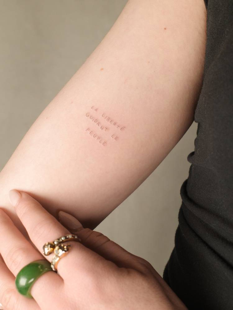 "La Liberté guidant le peuple" lettering tattoo placed on the inner forearm.