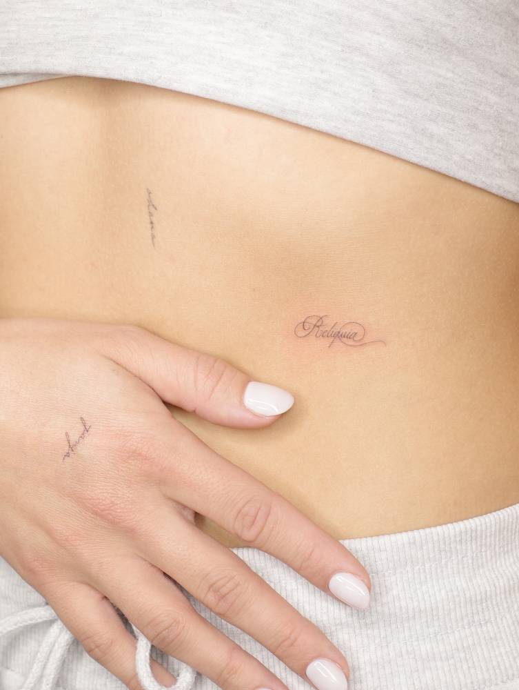 "Reliquia" lettering tattoo in script font located on the rib.