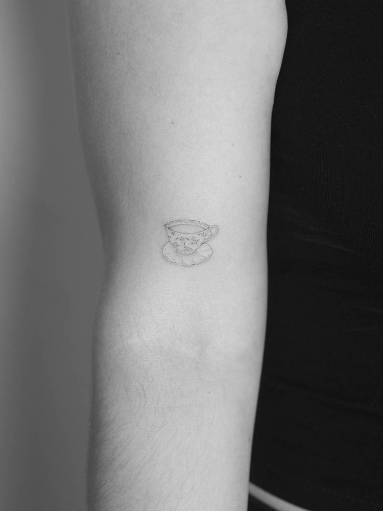 Little teacup in fine line style tattooed on the bicep.
