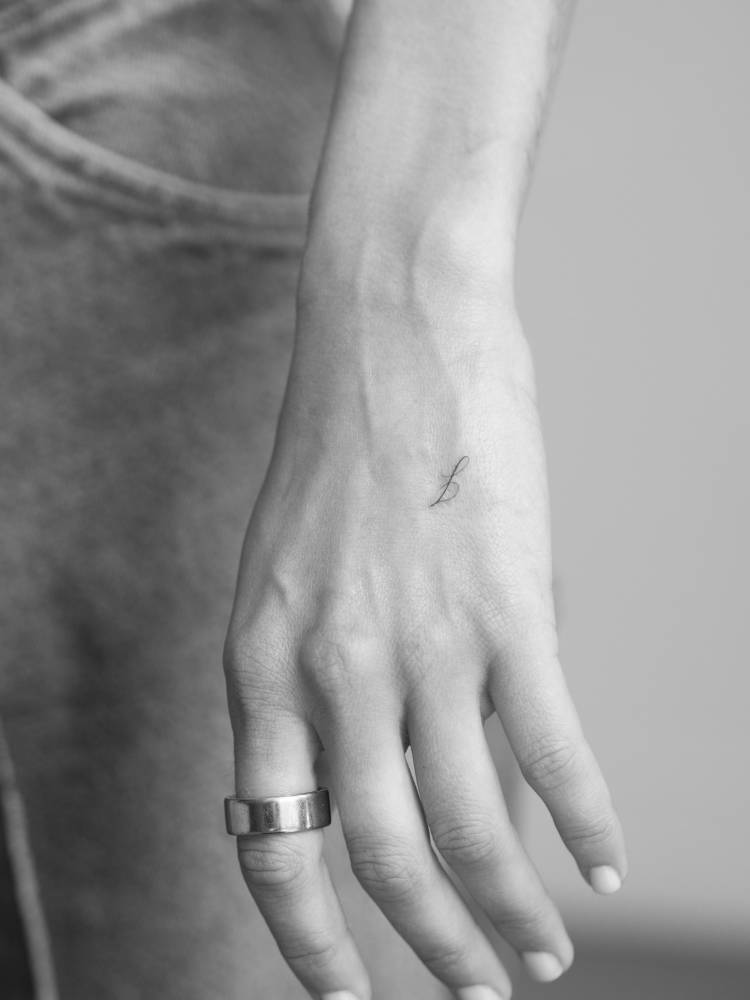 Little tattoo of the letter "J" in script font located on the hand.