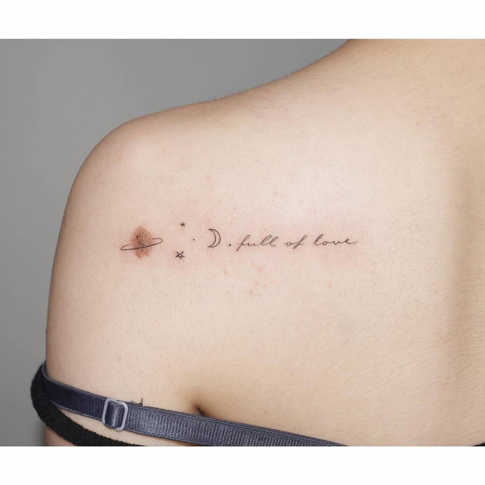 Saturn, stars, moon and words "full of love" tattooed on the shoulder blade.