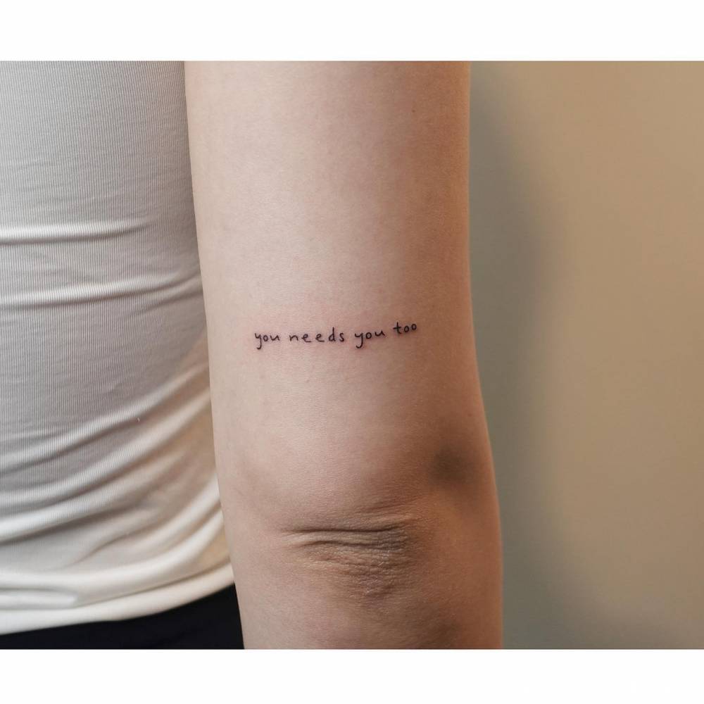 Handwritten font "you needs you too" lettering tattoo located on the tricep.