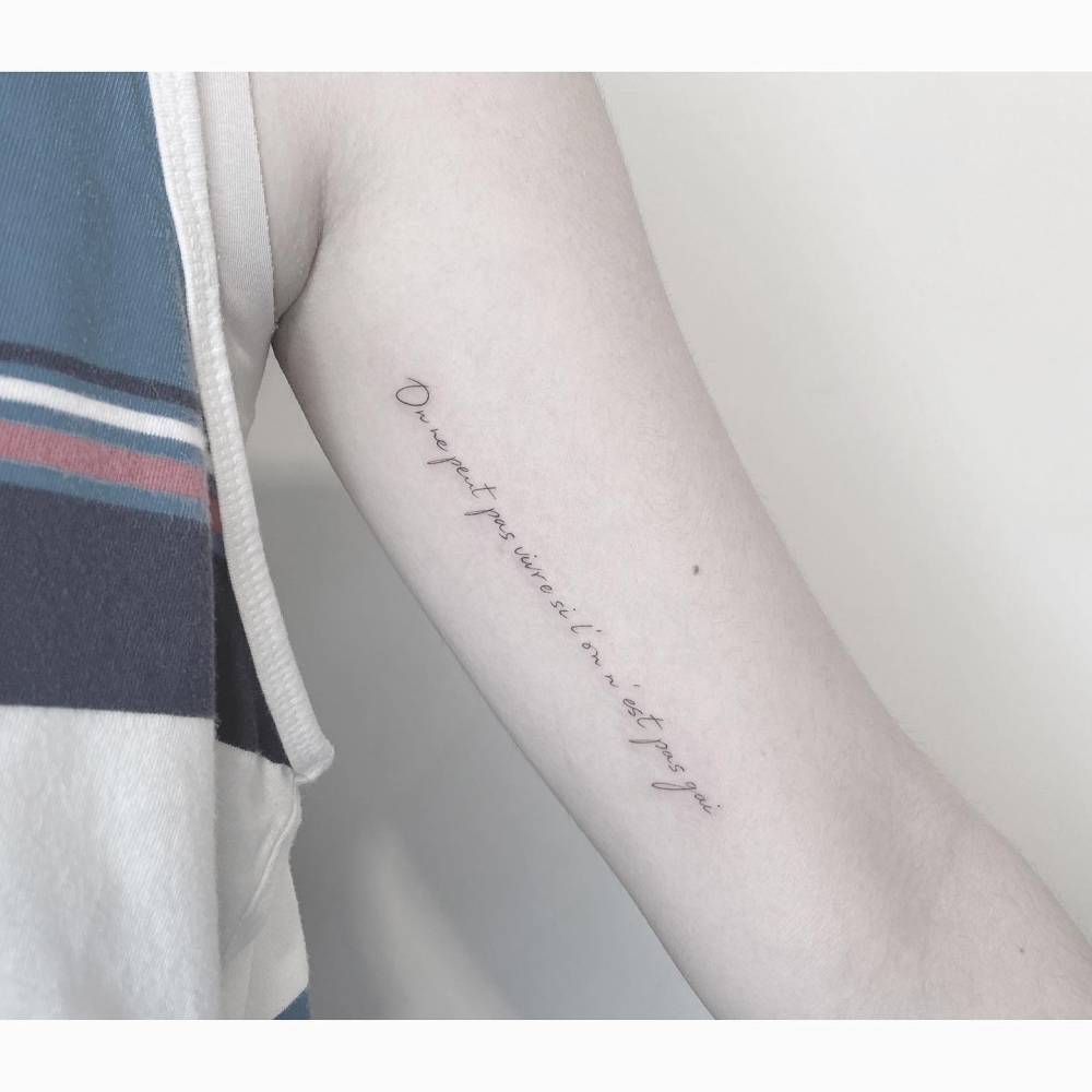 "On ne peut pas vivre si l'on n'est pas gai" lettering tattoo handwritten on the inner arm.