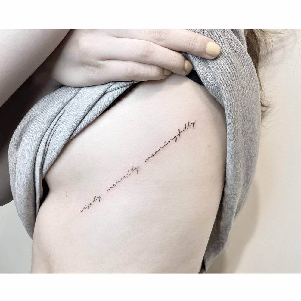 "Wisely, merrily meaningfully" lettering tattoo located on the rib.