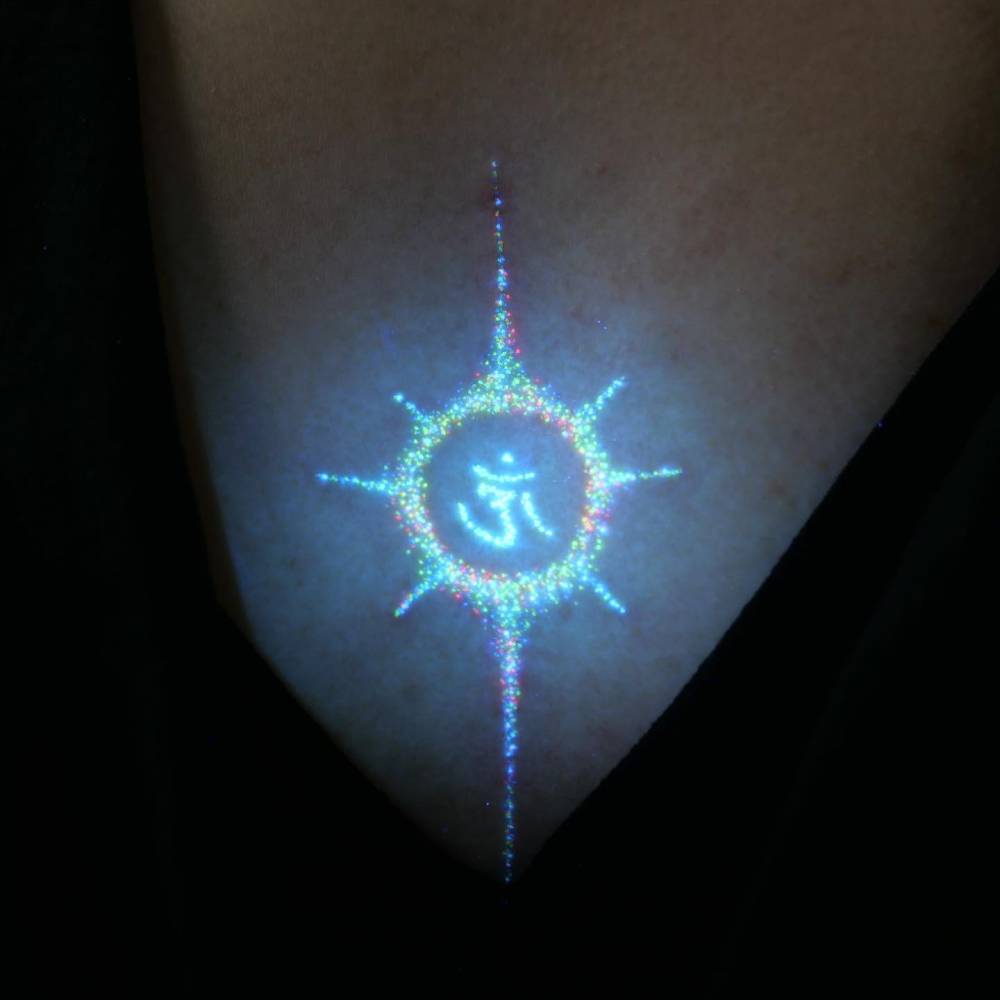 Glitter effect Om tattoo located on the chest.