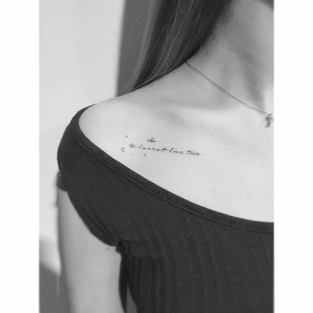 "Luceat lux tua" lettering tattoo located on the collarbone.