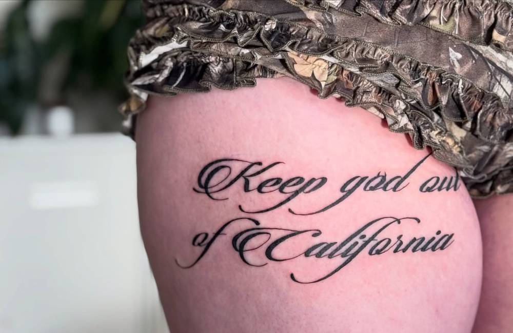 "Keep God out of California" lettering tattoo located on the thigh.