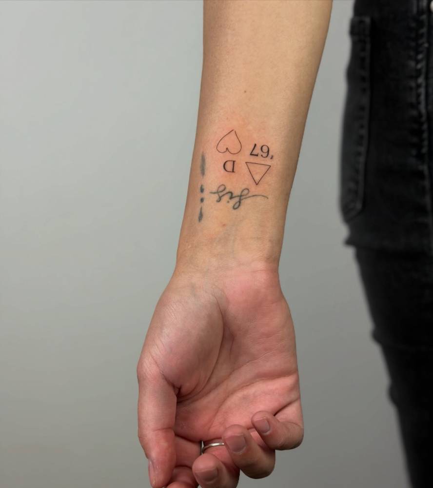 Letter "D", heart, triangle and number "67" tattooed on the wrist.