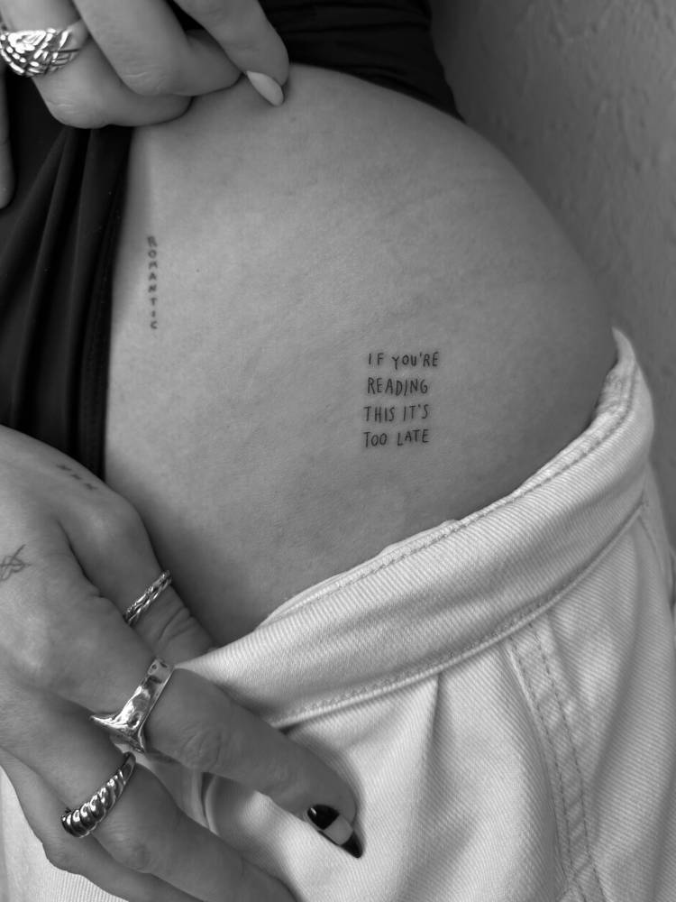 "If you're reading this it's too late" lettering tattoo located on the hip.