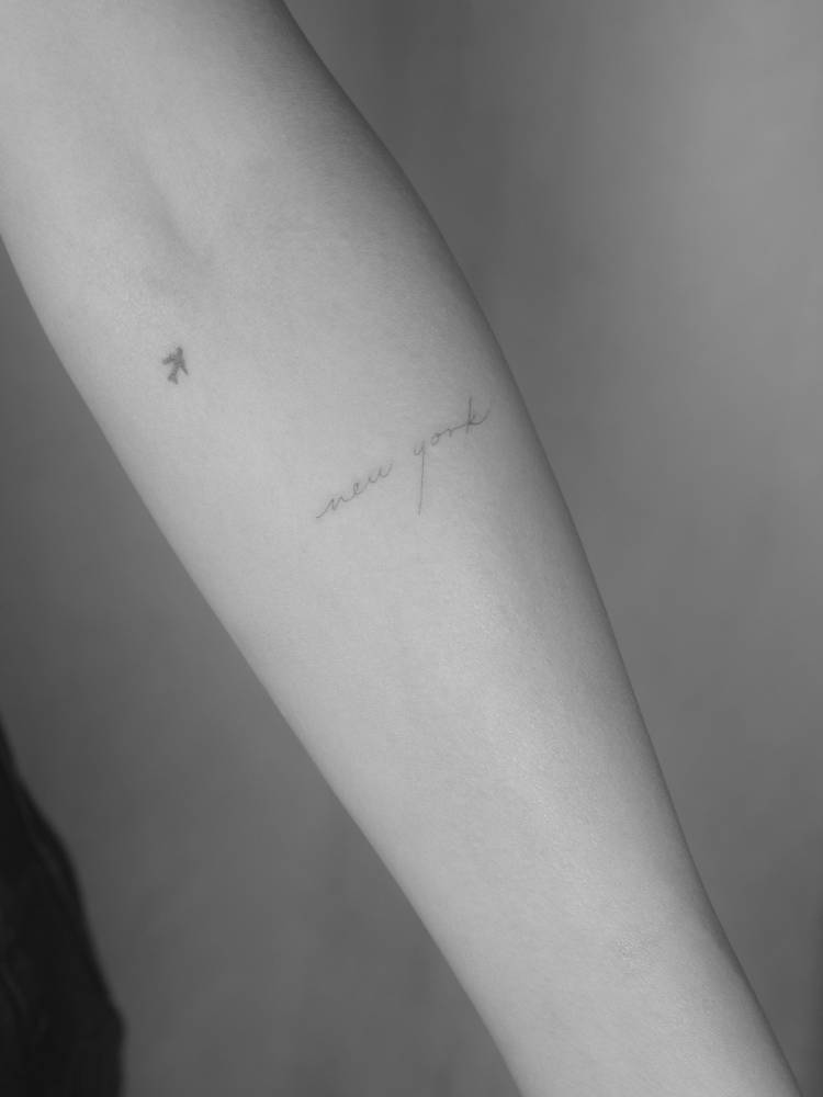 Handwritten font "New York" lettering tattoo placed on the inner forearm.