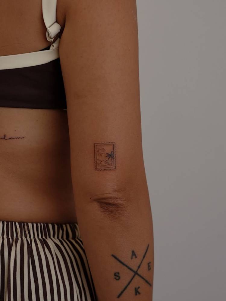 Fine line style beach stamp tattoo located on the tricep.