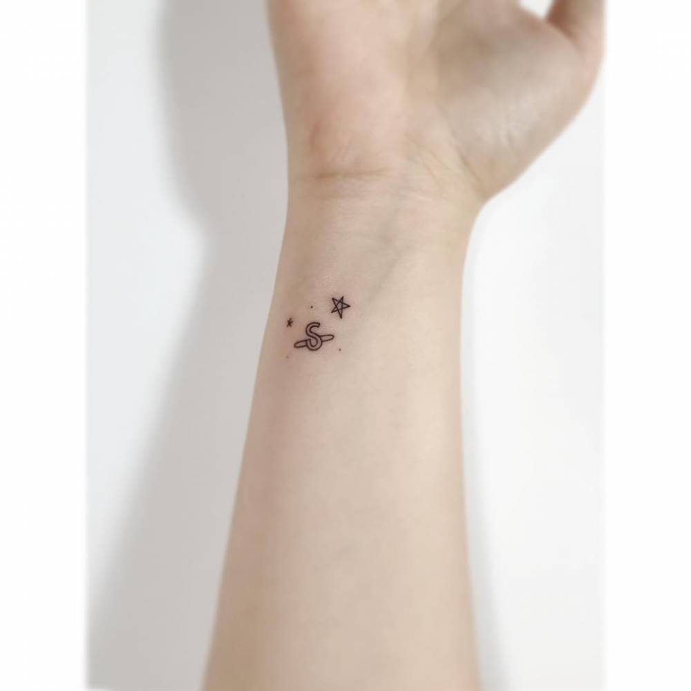 Letter "S" Saturn and stars tattooed on the wrist minimalistic style.