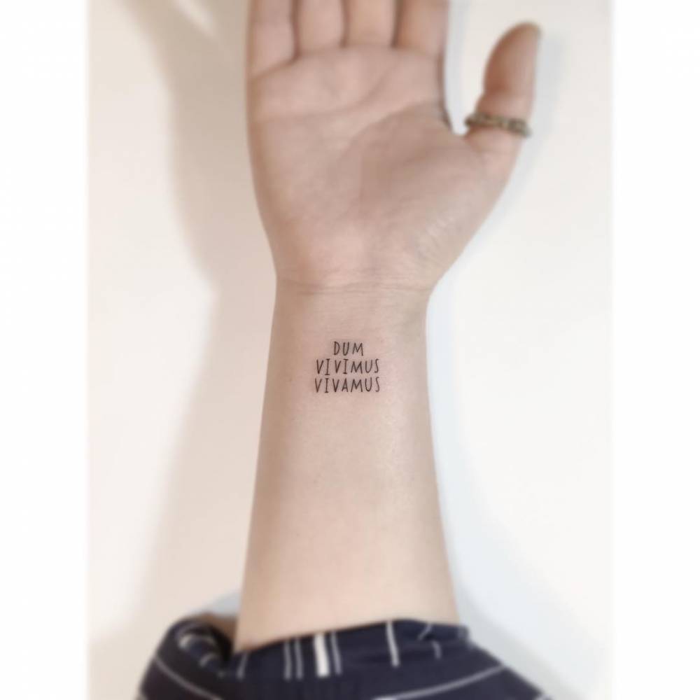 "Dum vivimus vivamus" lettering tattoo located on the wrist.