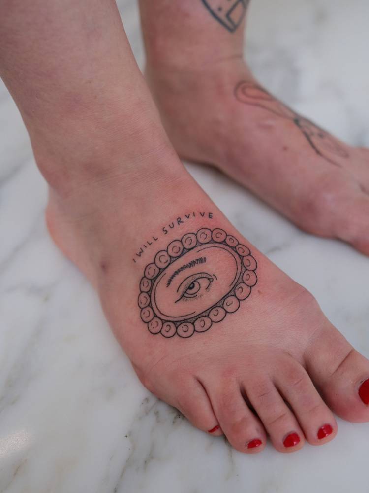 "I will survive" and eye tattoo located on the foot.
