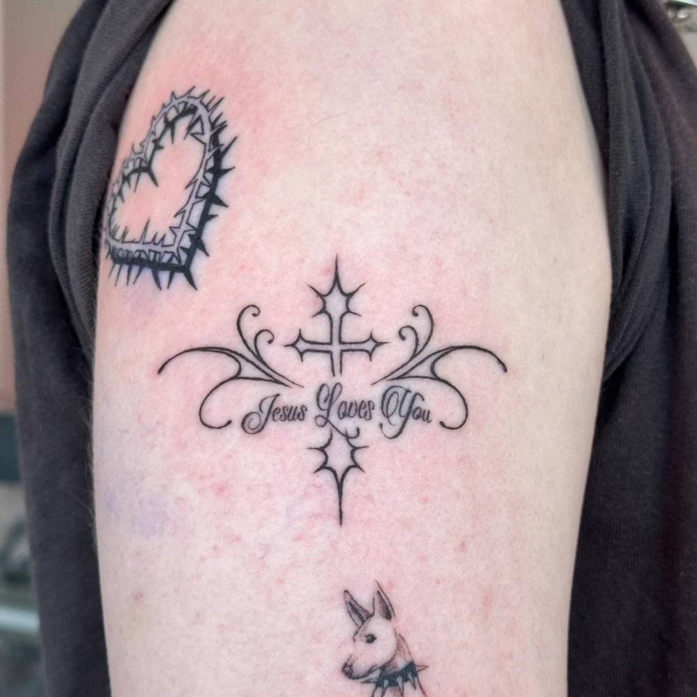 "Jesus loves you" and cross tattoo located on the upper arm.