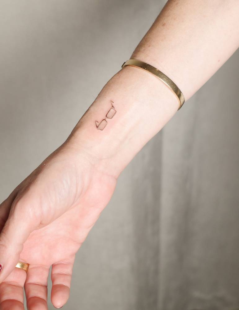 Fine line style eyeglasses tattoo located on the wrist.