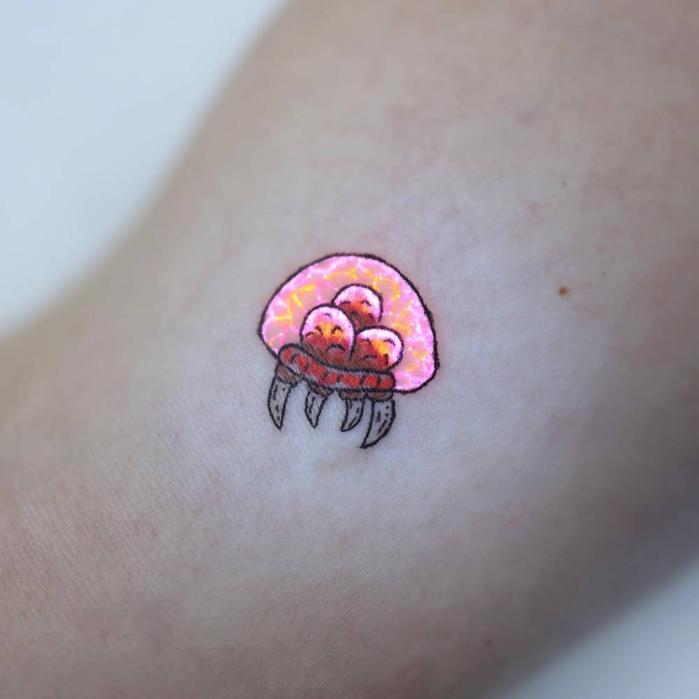 Metroid larva tattooed on the inner arm, cartoon style.