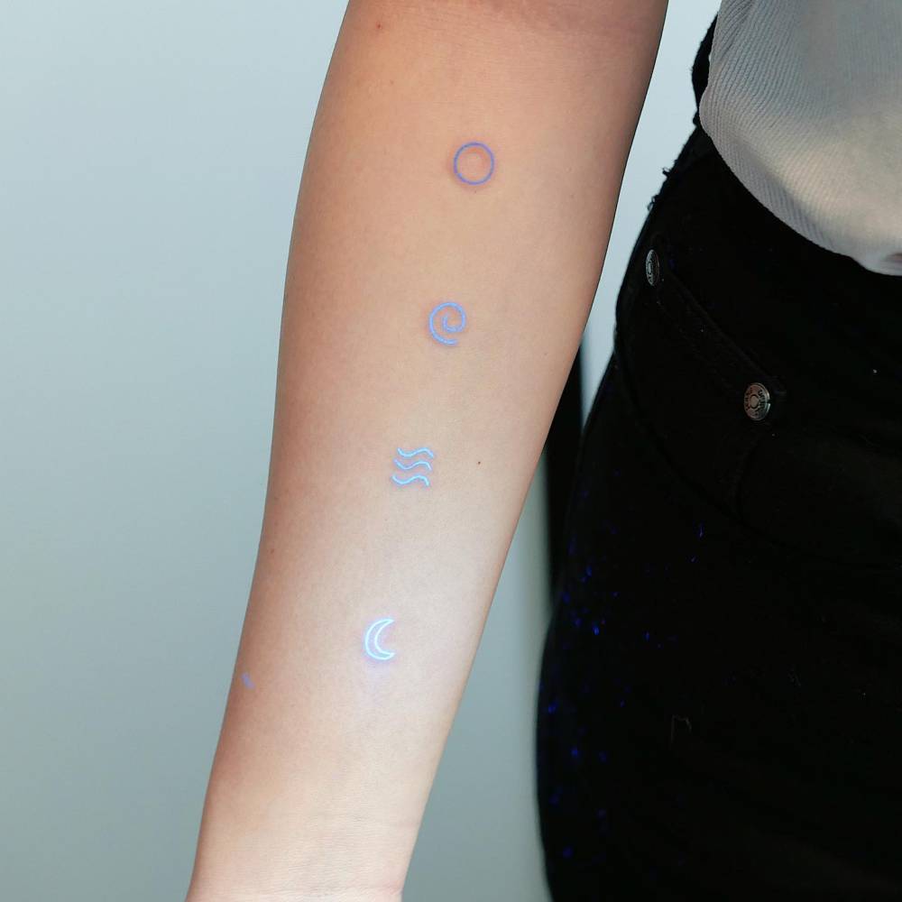 Tiny symbols in UV ink tattooed on the inner forearm.