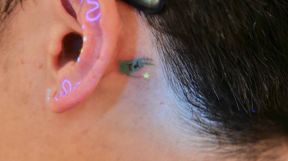 Plankton tattoo in cartoon style located behind the ear.